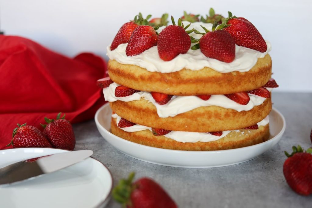 A strawberry shortcake with a white dessert plate next to it