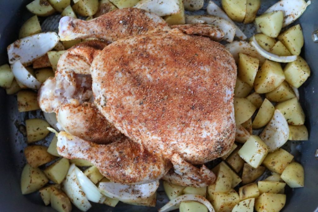 Roasting pan of an uncooked whole chicken with blackening spices and potatoes