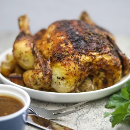Vertical image of a roasted blackened chicken on a plate with carving knfe
