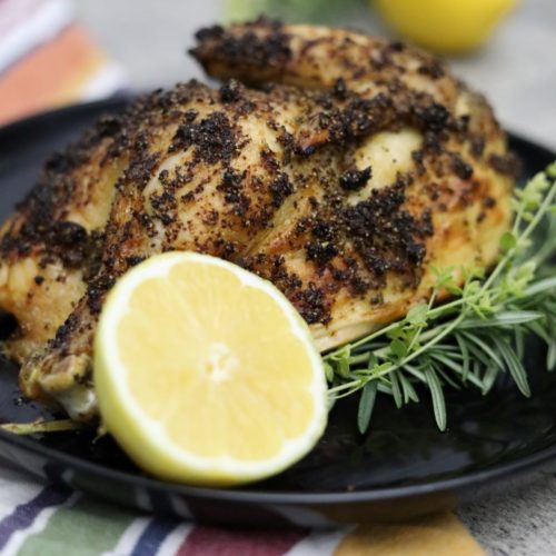 roasted half chicken on a black plate with lemon and herbs