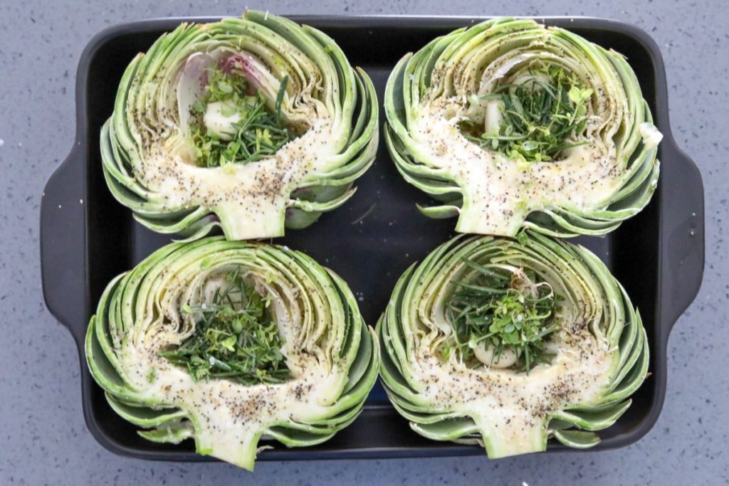 Artichoke halves filled with herbs and garlic in a baking dish