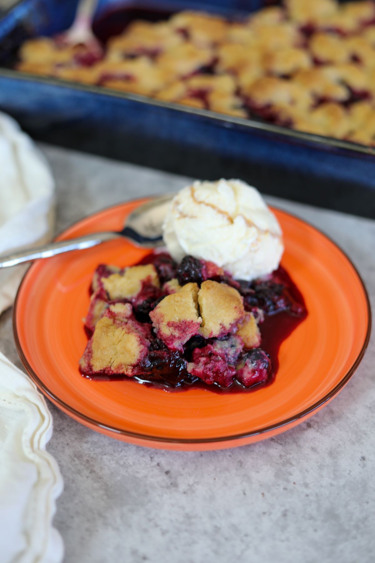 berry cobbler on an orange plate with a scoop of ice cream