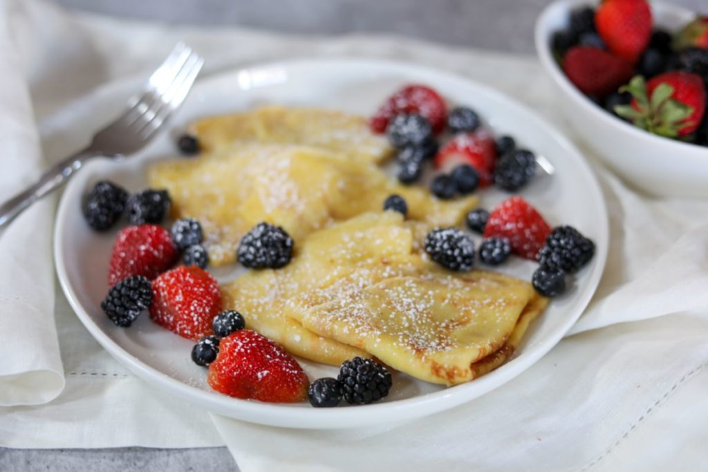 folded crepes with a bowl of fresh berries