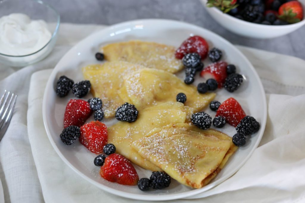 white plate with folded crepes and fresh fruit