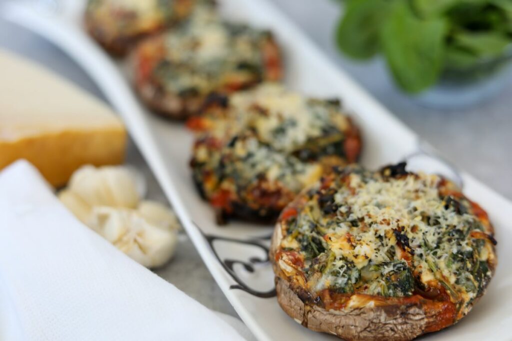 Three stuffed portobello mushrooms on a white and sliver tray next to garlic and a block of parmesan cheese.
