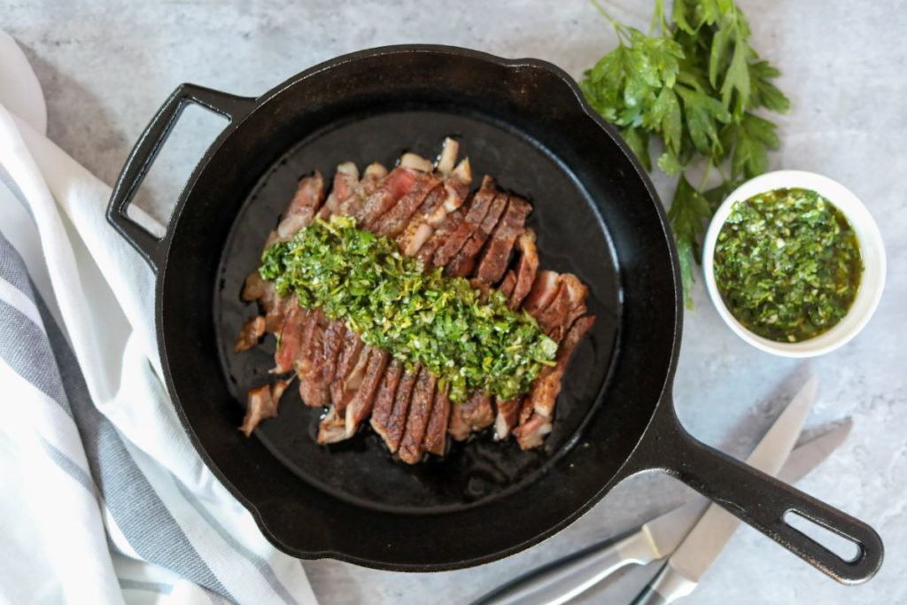 sliced steak with chimichurri sauce in a cast iron skillet