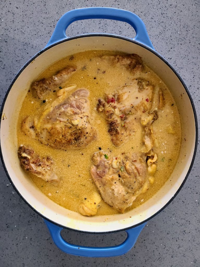 chicken thighs in coconut sauce in a blue Dutch oven