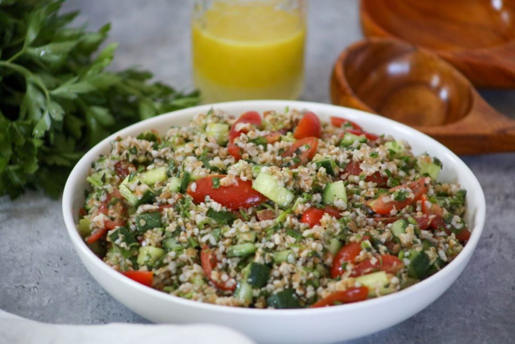 A bowl of tabbouleh with dressing behind it