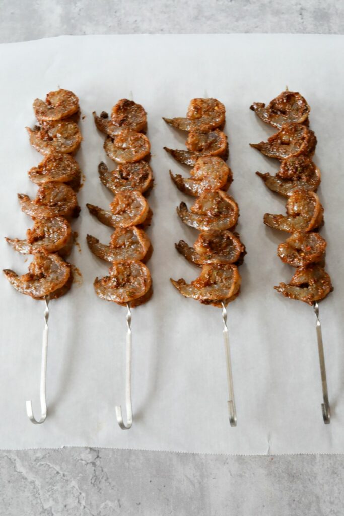 Four metal skewers with shrimp on them