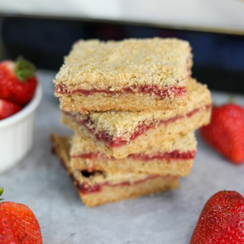 A stack of strawberry crumble bars surrounded by fresh strawberries