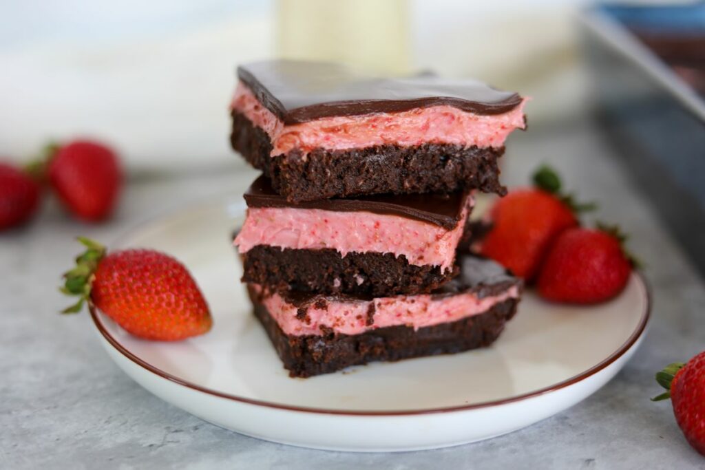 A stack of three strawberry brownies on a white plate with strawberries