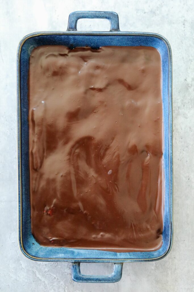 chocolate ganache layer of strawberry brownies in a blue baking dish