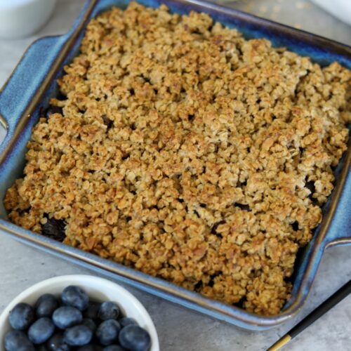 Blueberry crisp in a baking dish next to a cup of blueberries
