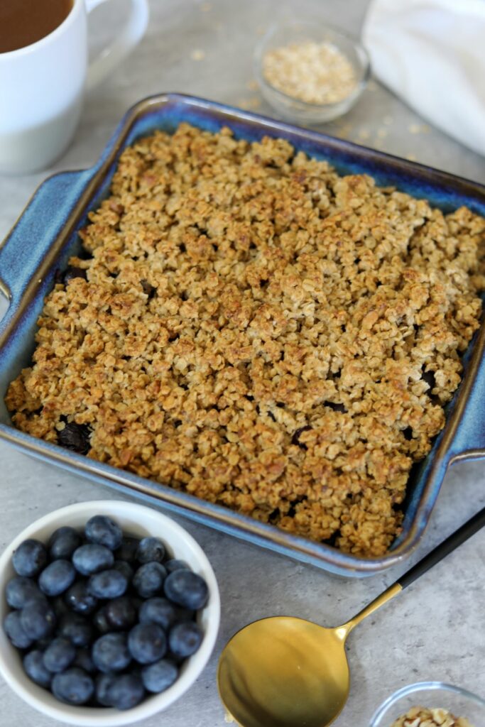 Blueberry crisp in a baking dish next to a cup of blueberries