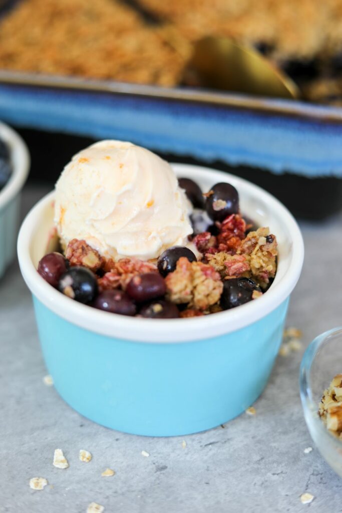 A cup of blueberry crisp with a scoop of ice cream on top