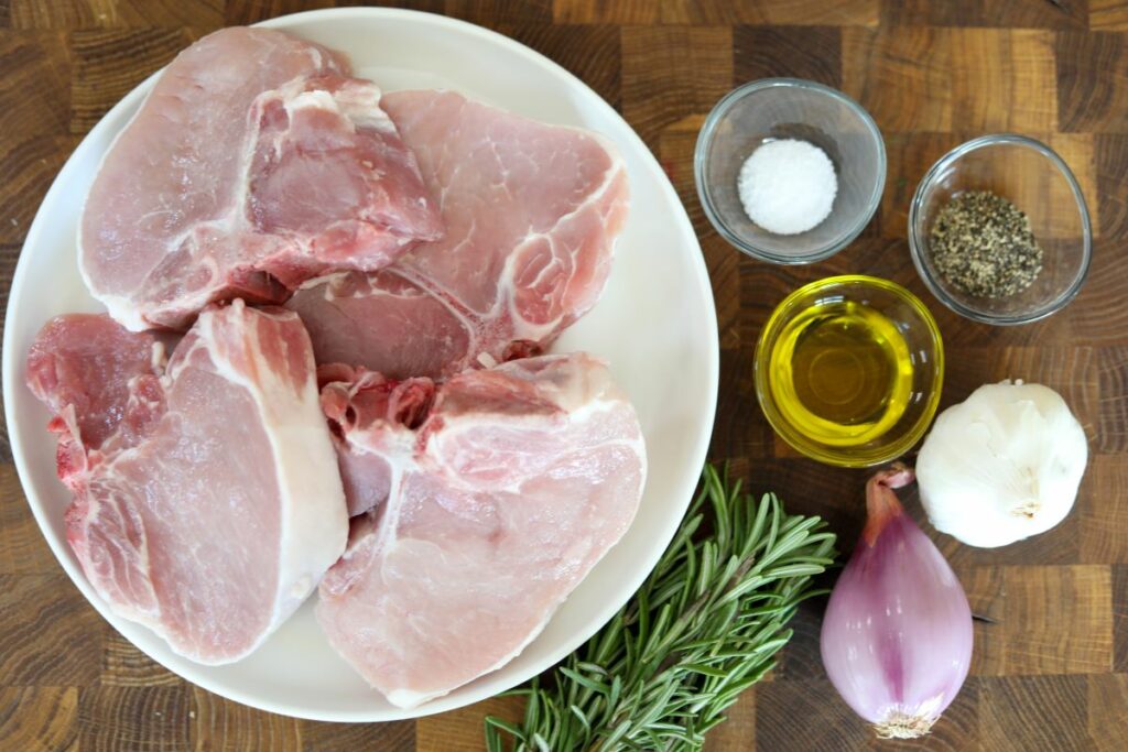 Ingredients for rosemary pork chops on a wooden cutting board