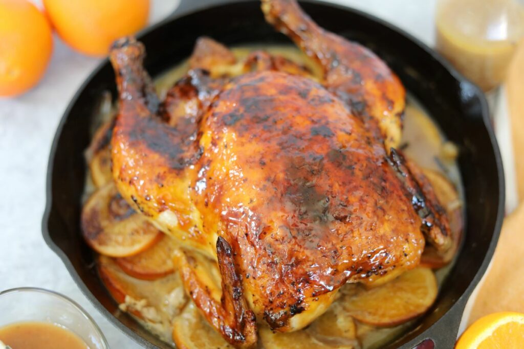 Whole chicken on a bed of orange and onions in a cast iron skillet