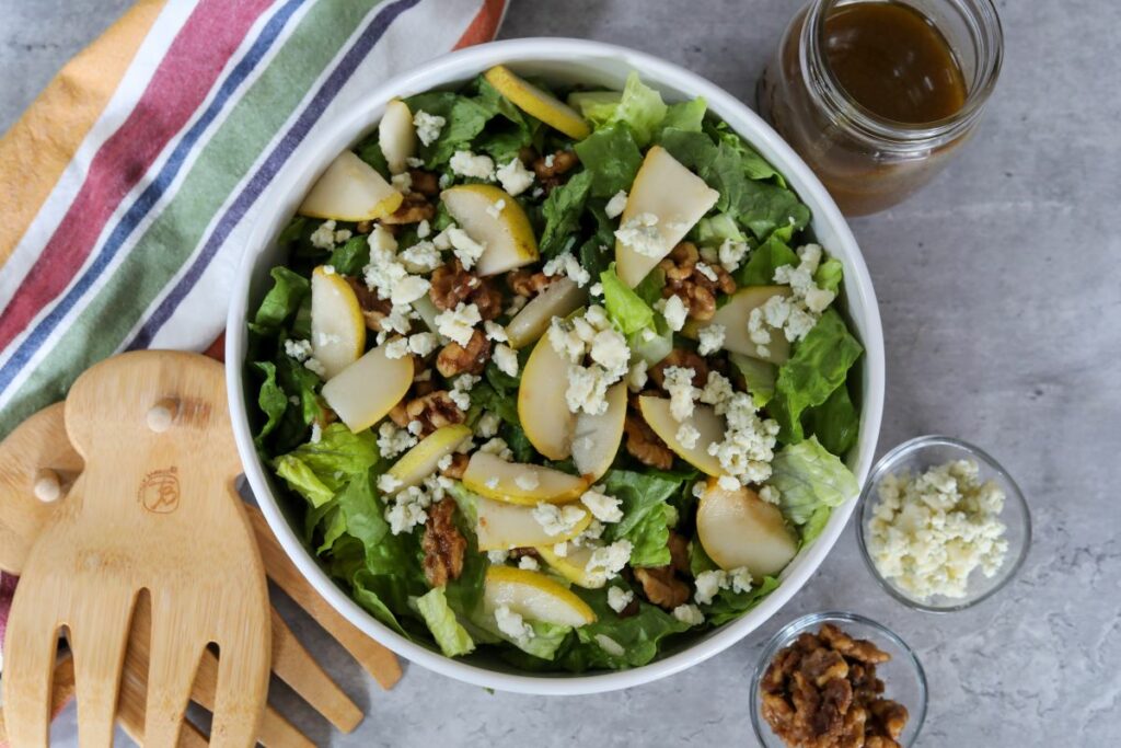 A white bowl with pear salad and salad tongs