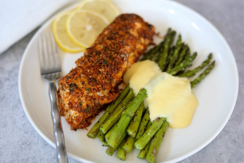 A fillet of fish on a white plate with hollandaise asparagus
