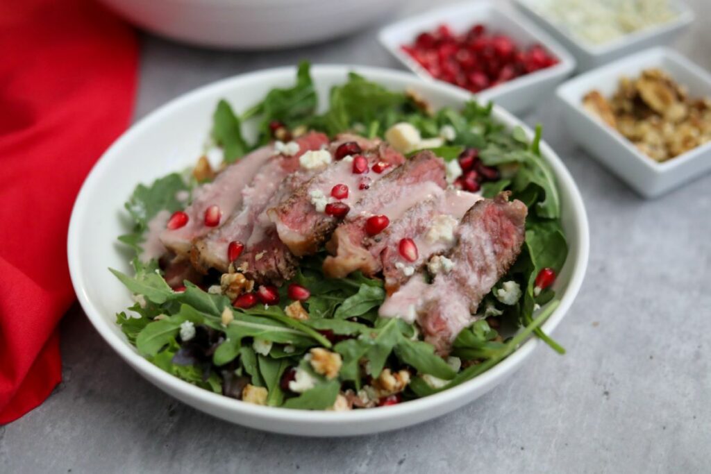 Dressed pomegranate steak salad in a shallow bowl