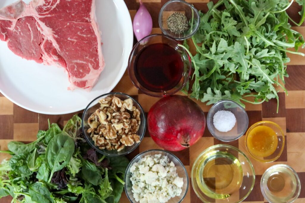 Ingredients for pomegranate steak salad on a wooden cutting board