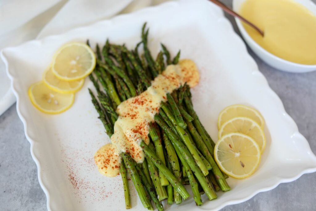 Roasted asparagus on a white platter with hollandaise on it