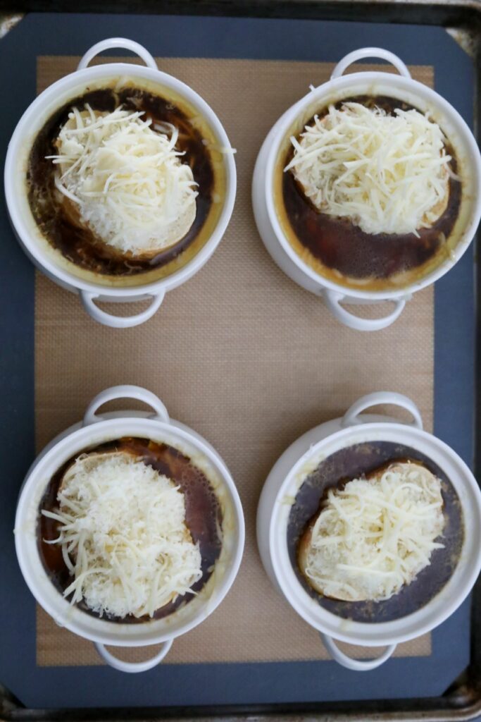 Four bowls of French onion soup with cheese on bread ready to be broiled