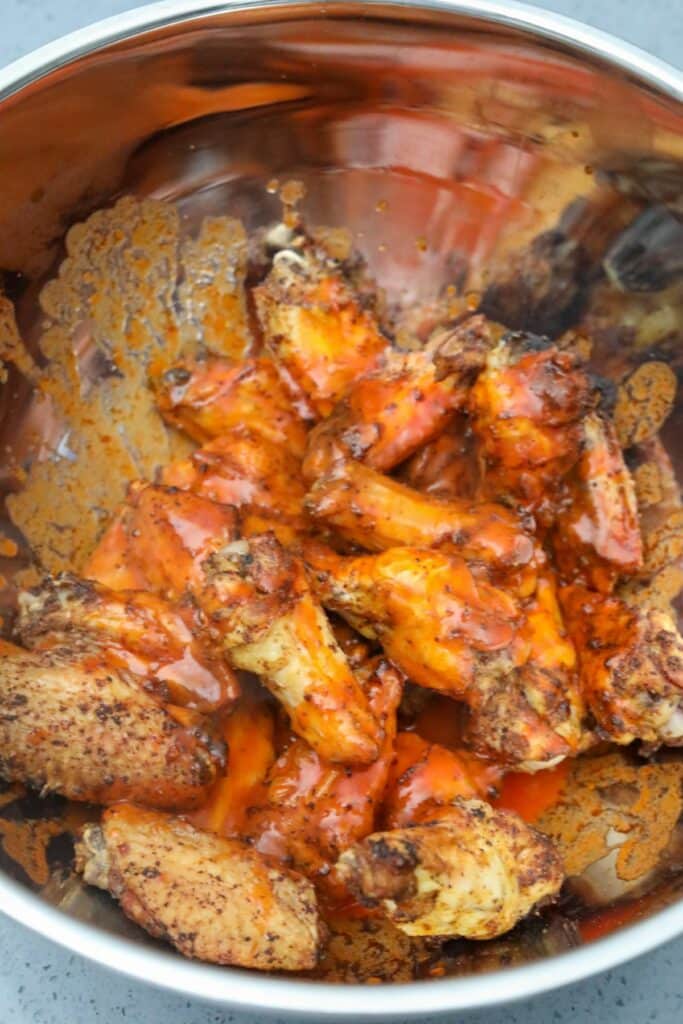 A metal bowl with wings and buffalo sauce
