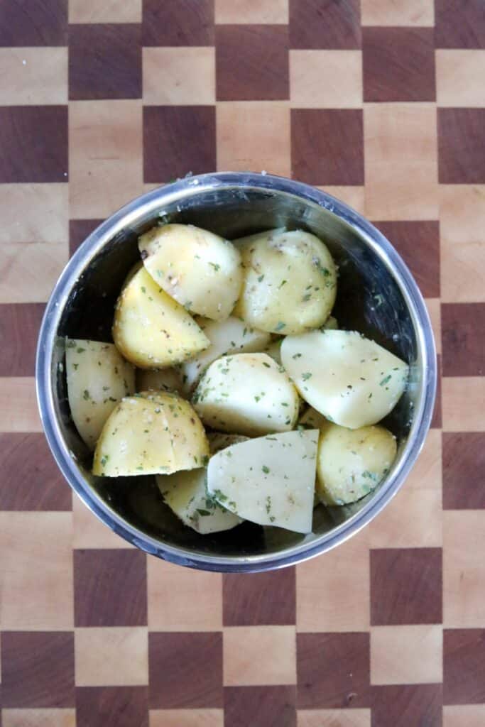 A bowl of sliced potatoes coated in butter and herbs