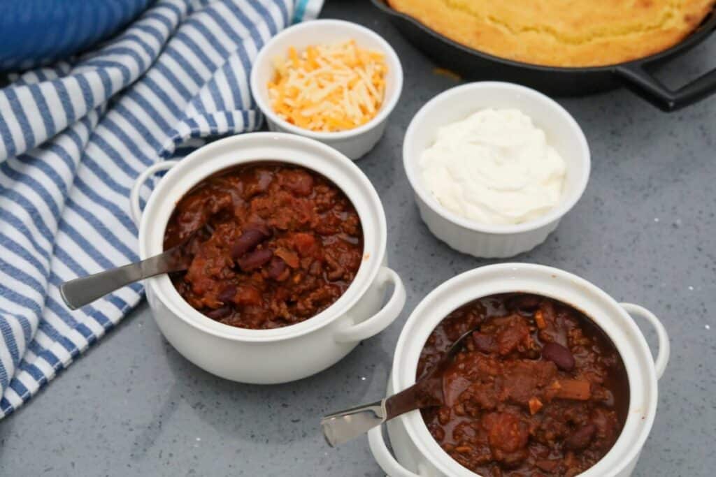 Two white soup crocks with classic chili and toppings