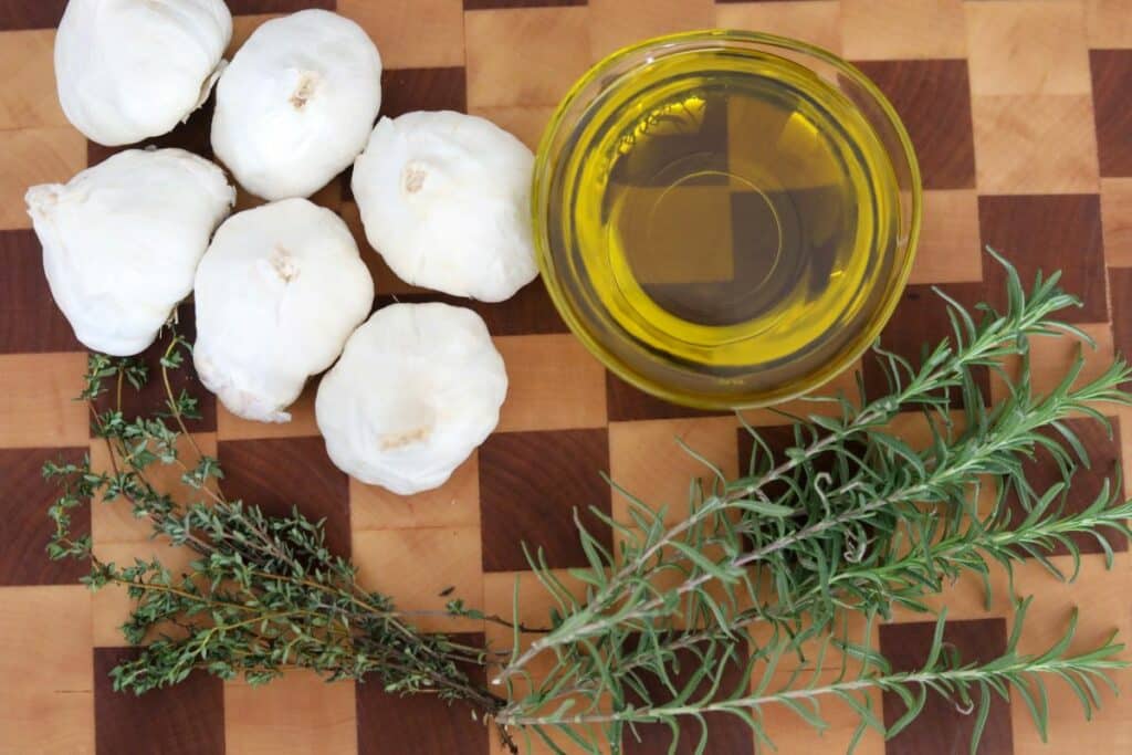 Ingredients for garlic confit on a wooden cutting board