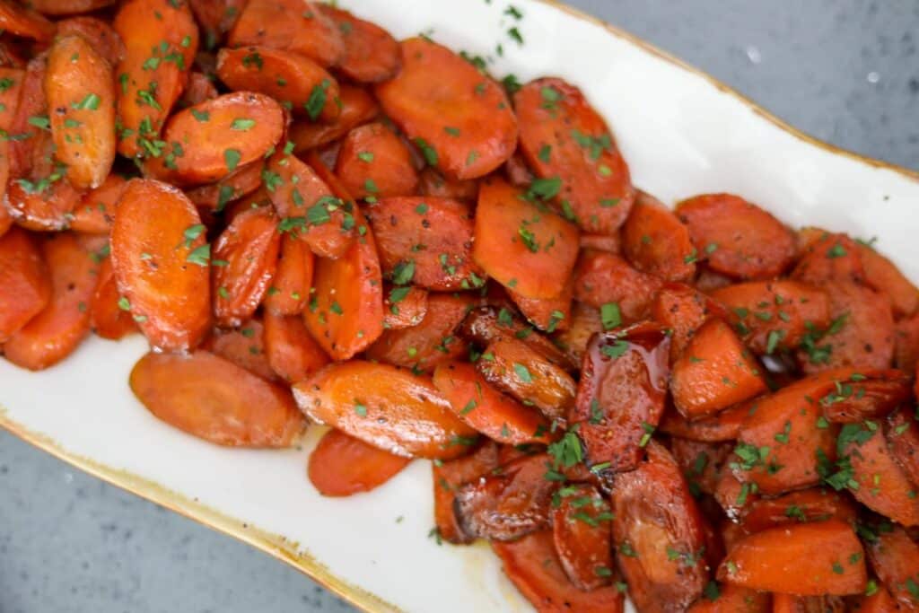 A gold and white platter with glazed carrots