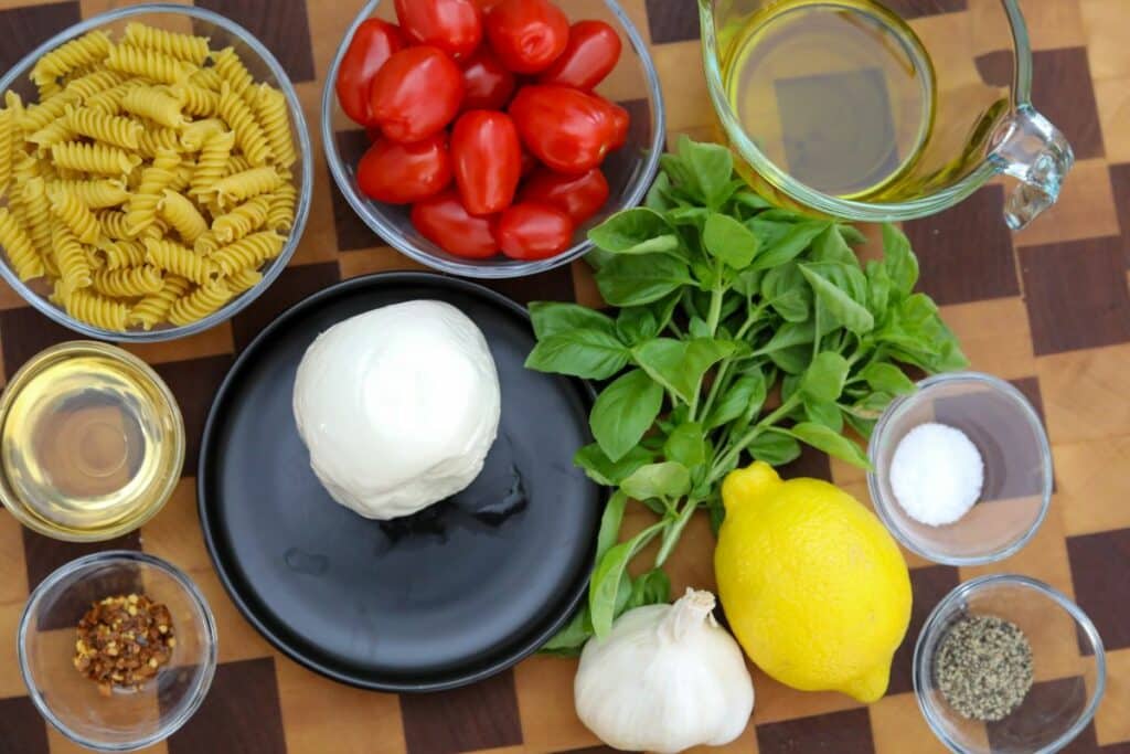 Ingredients for Caprese pasta salad on a wooden cutting board