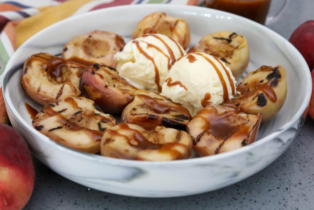 grilled peaches with caramel sauce in a bwol with scoops of ice cream
