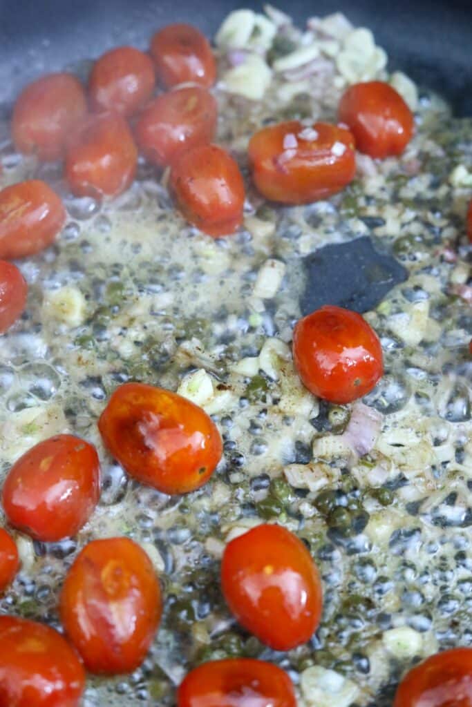 Blistered tomatoes, garlic, shallots, and capers in a pan