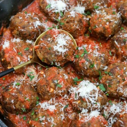 A cast iron skillet with Italian meatballs in tomato sauce with a spoon under a meatball